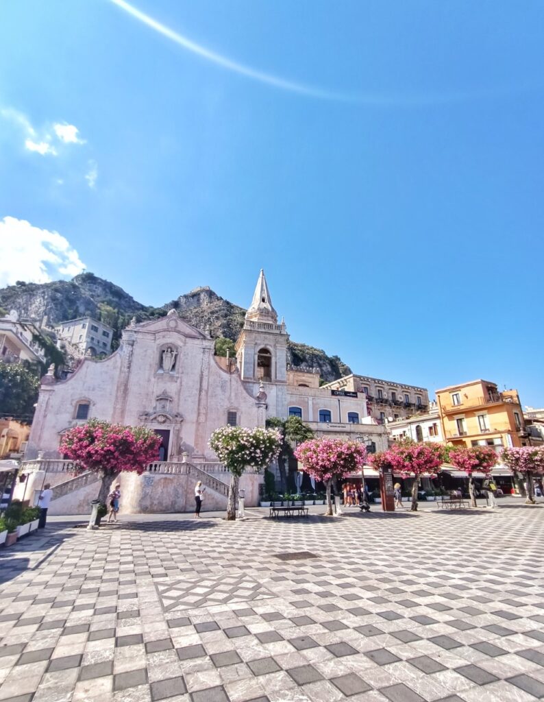 wide angle photo of piazza ix aprile in taormina sicily, with the pink church and flower trees