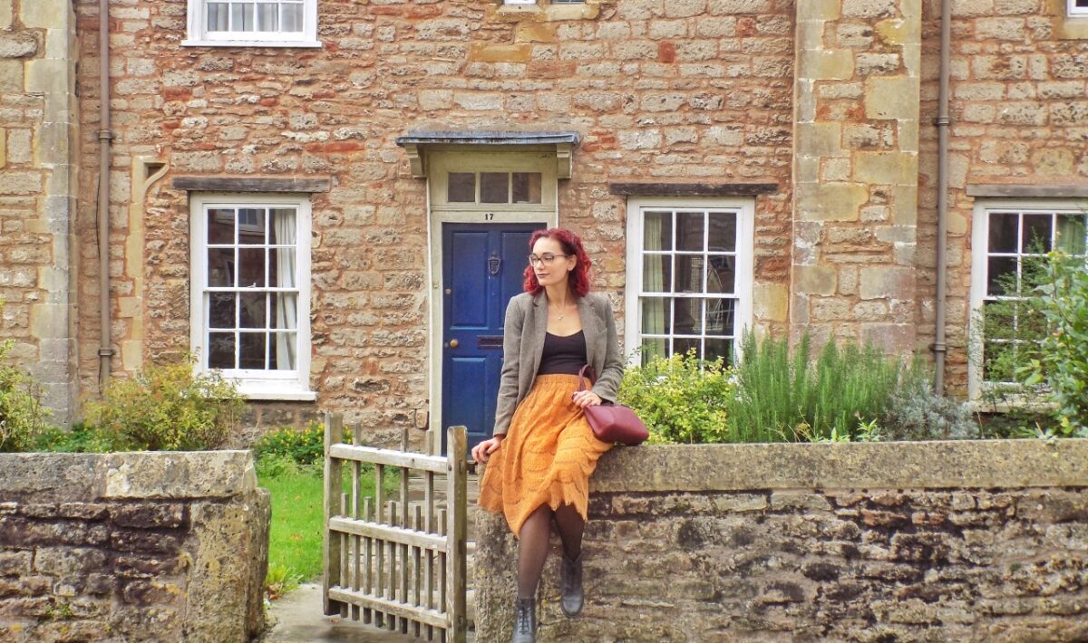 girl wearing an autumn outfit standing in front of a cottage in Wells, England