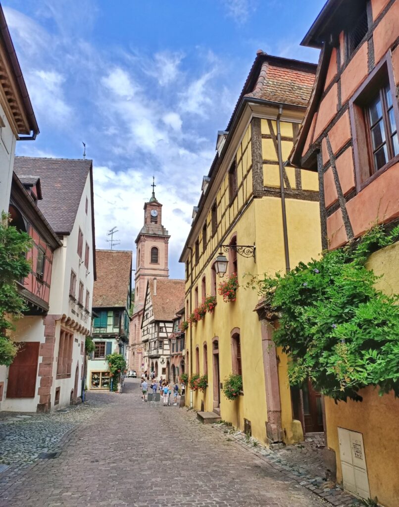 a colourful street with medieval buildings and the bell tower of a church