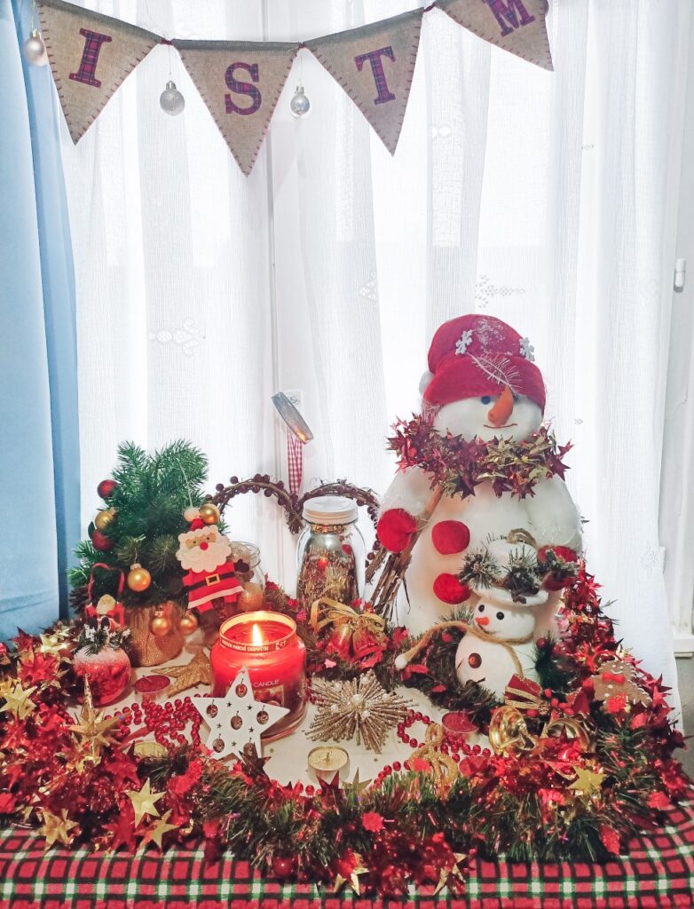 christmas display in front of window, with snowmen, garlands and christmas ornaments, burning candle