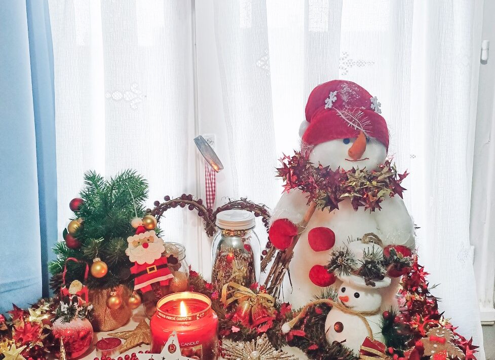 christmas display in front of window, with snowmen, garlands, christmas ornaments and candle burning