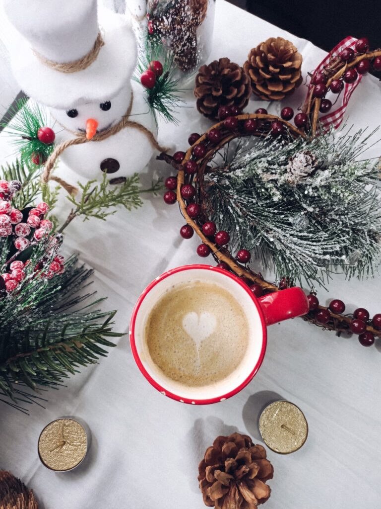 Flat lay with cup of coffee, winter decor with pine cones, pine branches, berries, snowman and candle