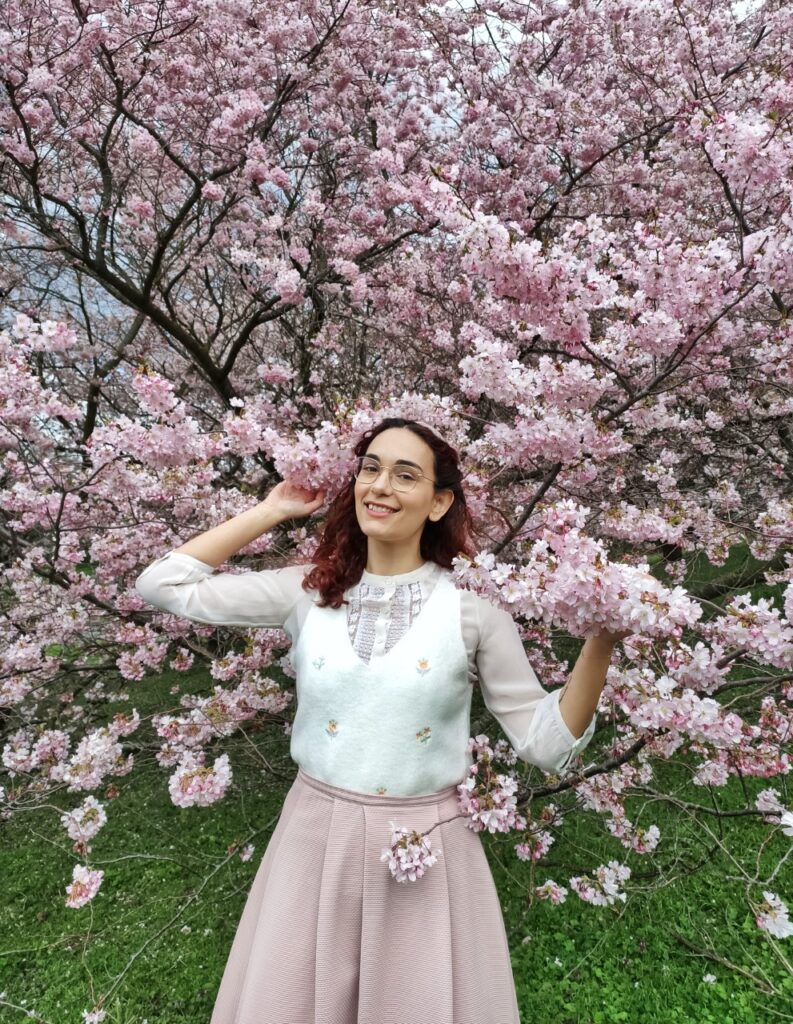I am standing in front of a big cherry blossom tree, hugging the branches around me. I am wearing a vintage-inspired outfit with pink and cream shades and little embroidered flowers.