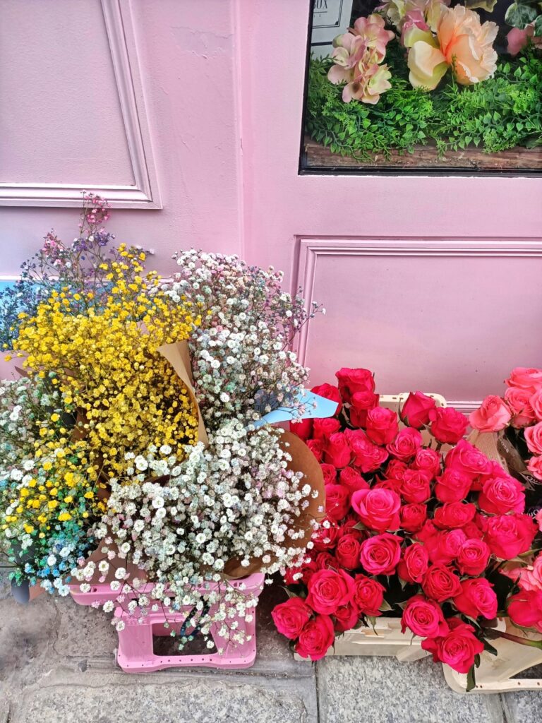 Boxes of colourful flowers in front of a flower shop in Paris, France. There is white, pink, yellow and blue gypsophila and bright pink roses.