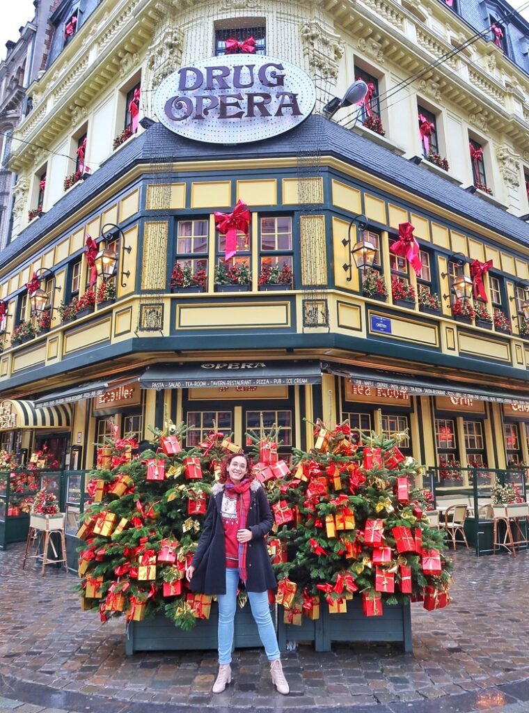 The festive Christmas decor at the Drug Opera restaurant in Brussels, Belgium. I am standing in front of Christmas trees decorated with red and yellow presents. There are big red bows at the windows.