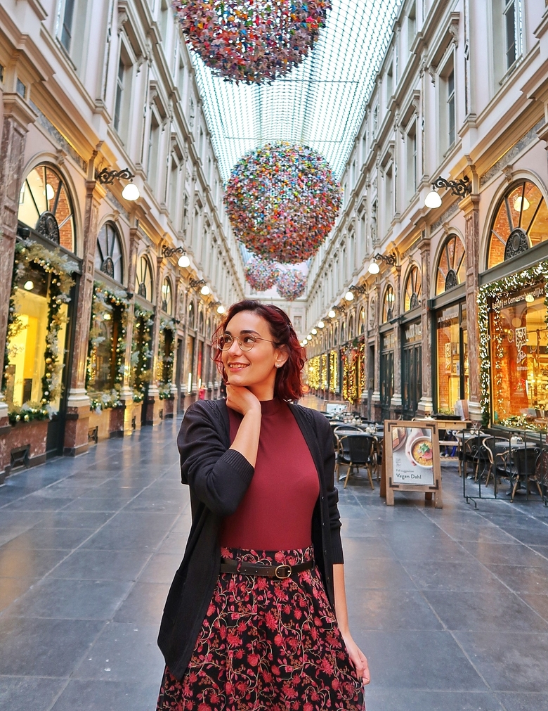I am standing in the Galeries Royales Saint Hubert, a covered arcade in Brussels, Belgium. There are Christmas lights in the background.