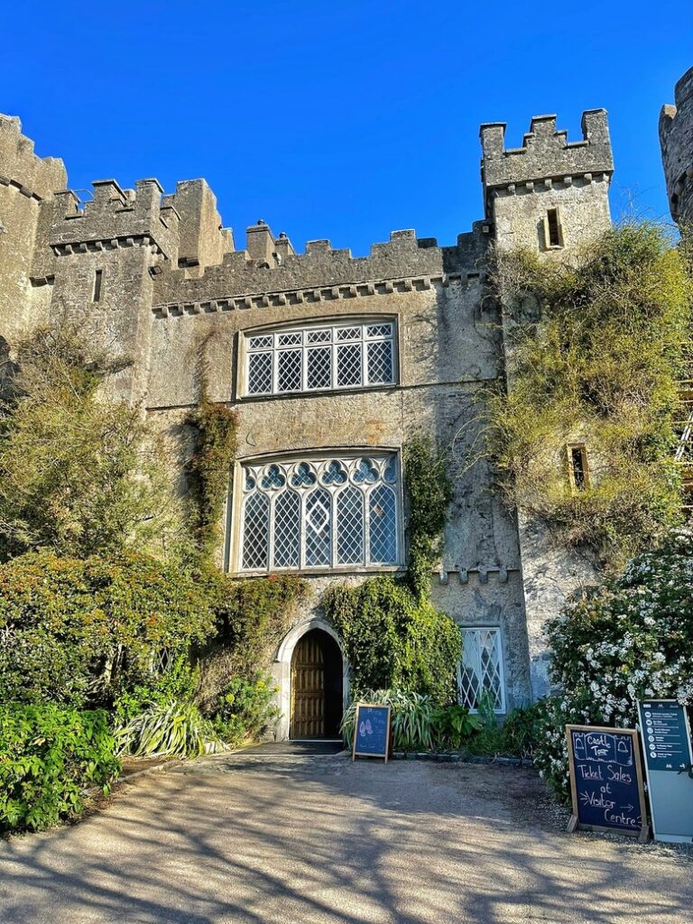 The green facade of Malahide Castle near Dublin, Ireland. The windows and walls are covered in leaves.